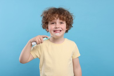 Cute little boy holding electric toothbrush on light blue background