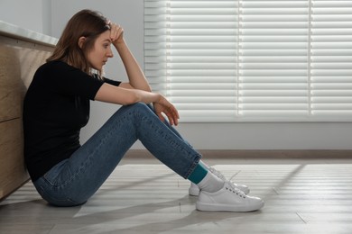 Photo of Sad young woman sitting on floor indoors, space for text