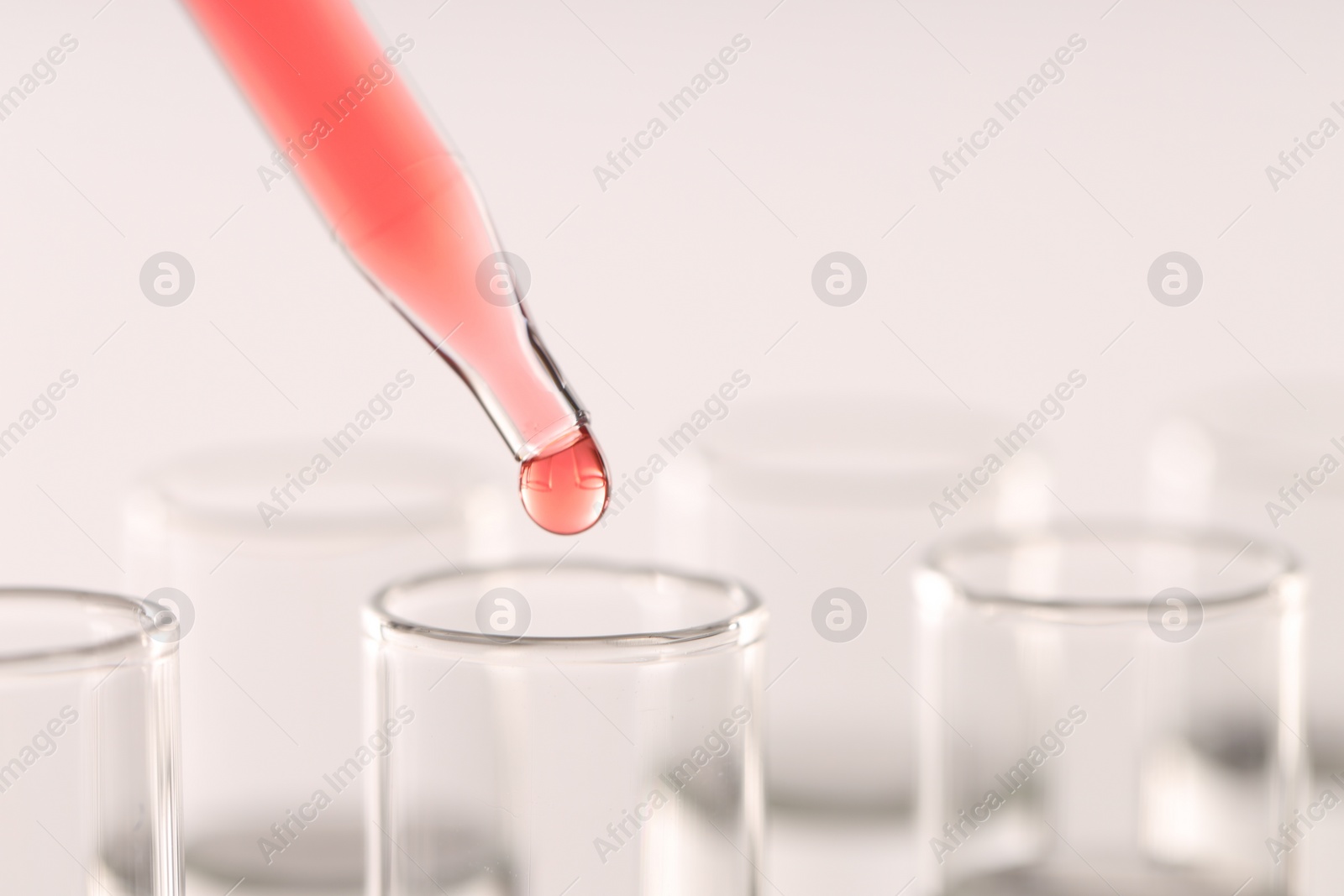 Photo of Dripping liquid from pipette into test tube on light background, closeup