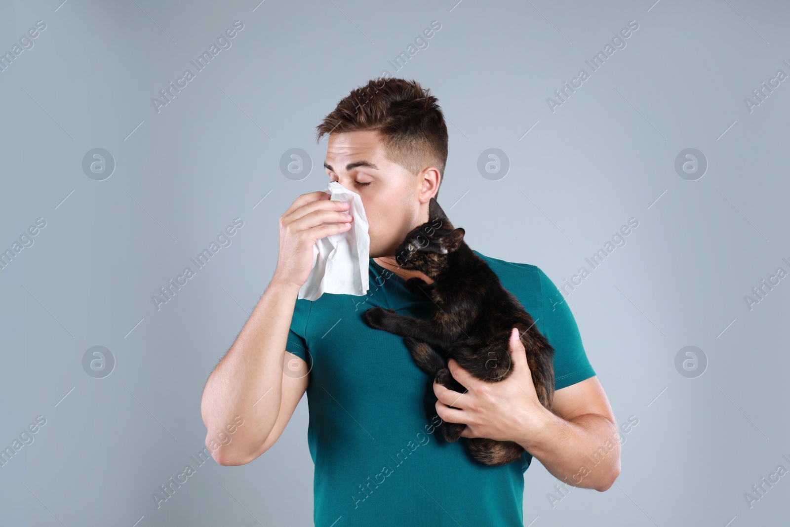 Photo of Young man with cat suffering from allergy on grey background