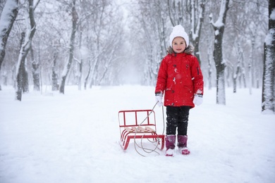 Photo of Cute little girl with sleigh outdoors on winter day, space for text