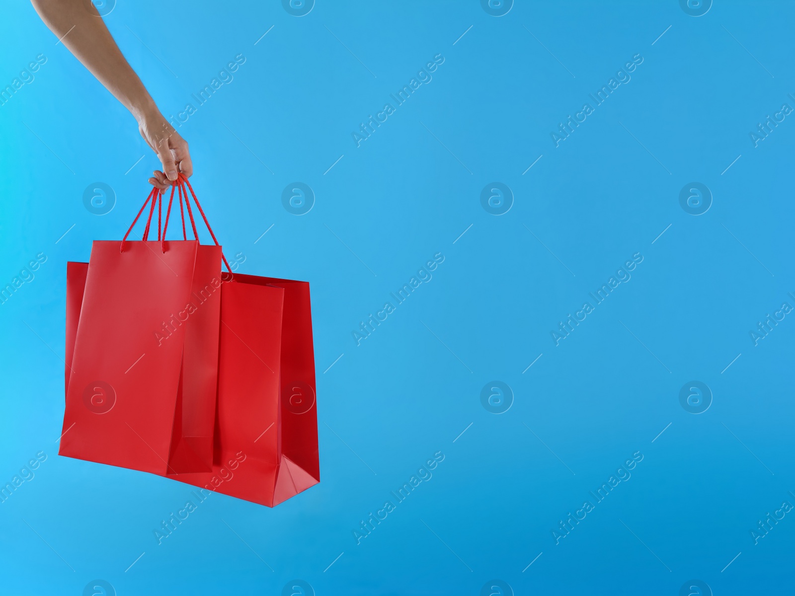 Photo of Woman with paper shopping bags on light blue background, closeup. Space for text