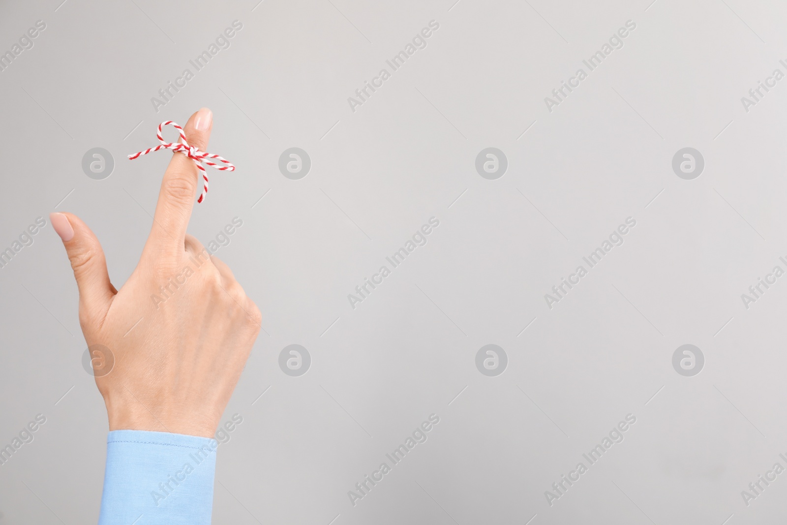 Photo of Woman showing index finger with tied bow as reminder on light grey background, closeup. Space for text