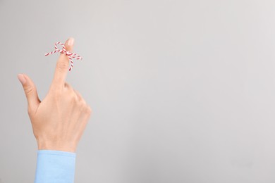 Woman showing index finger with tied bow as reminder on light grey background, closeup. Space for text