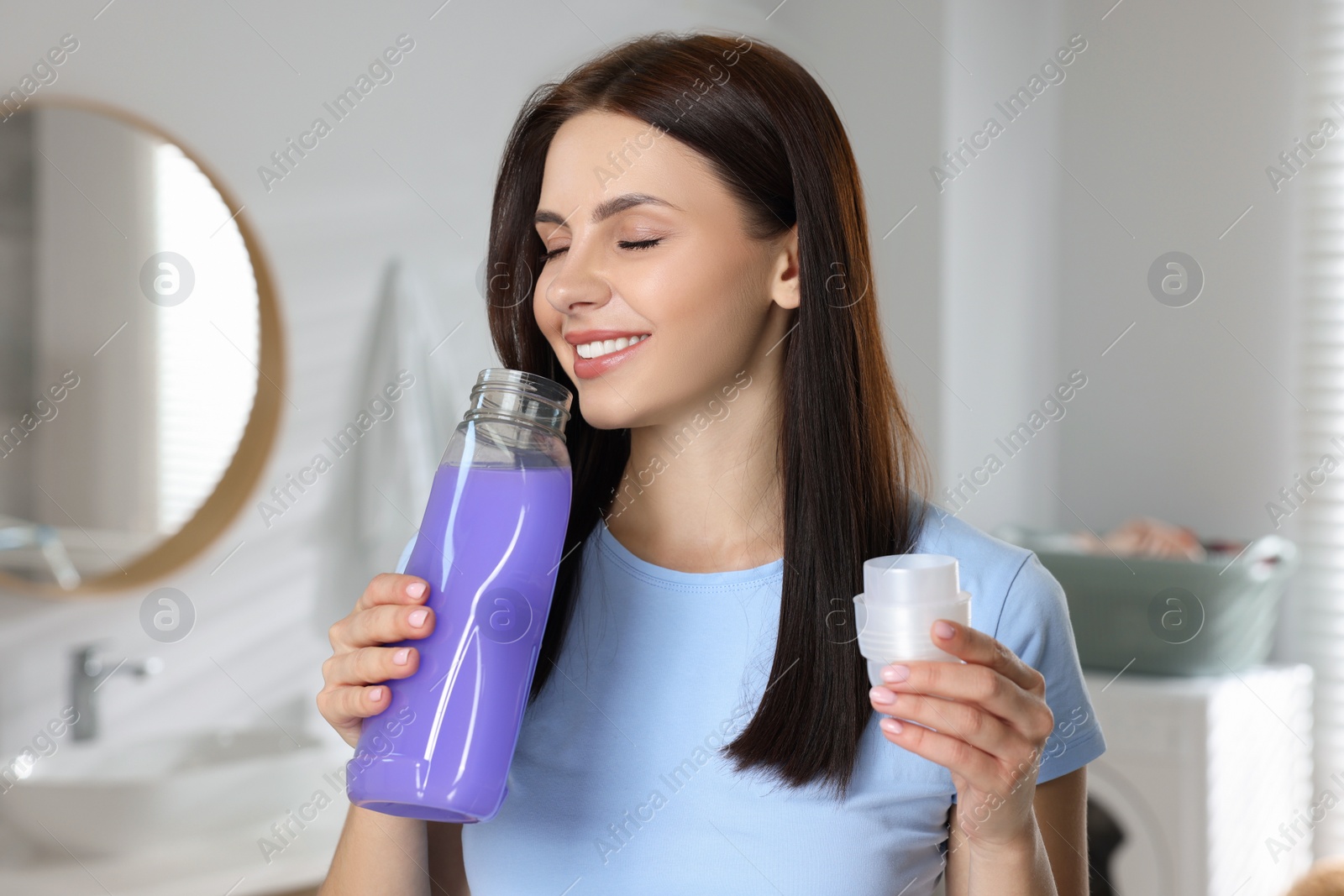 Photo of Woman smelling fabric softener in bathroom, space for text