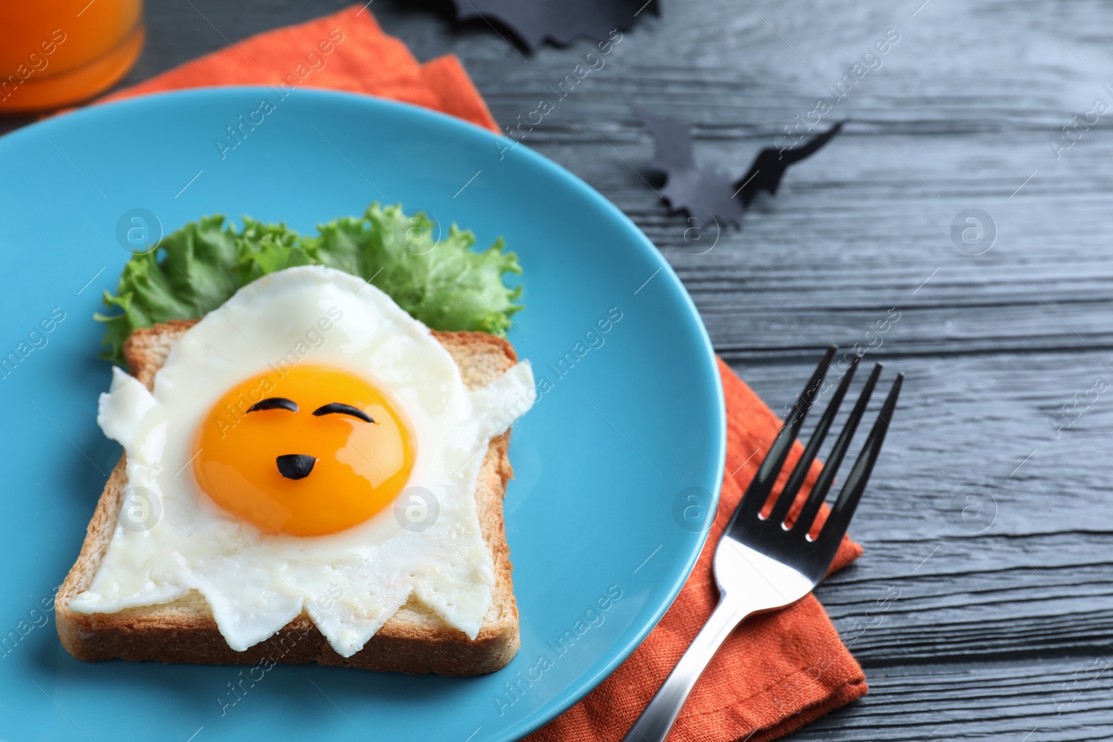 Photo of Halloween themed breakfast served on black wooden table, closeup. Tasty toast with fried egg in shape of ghost