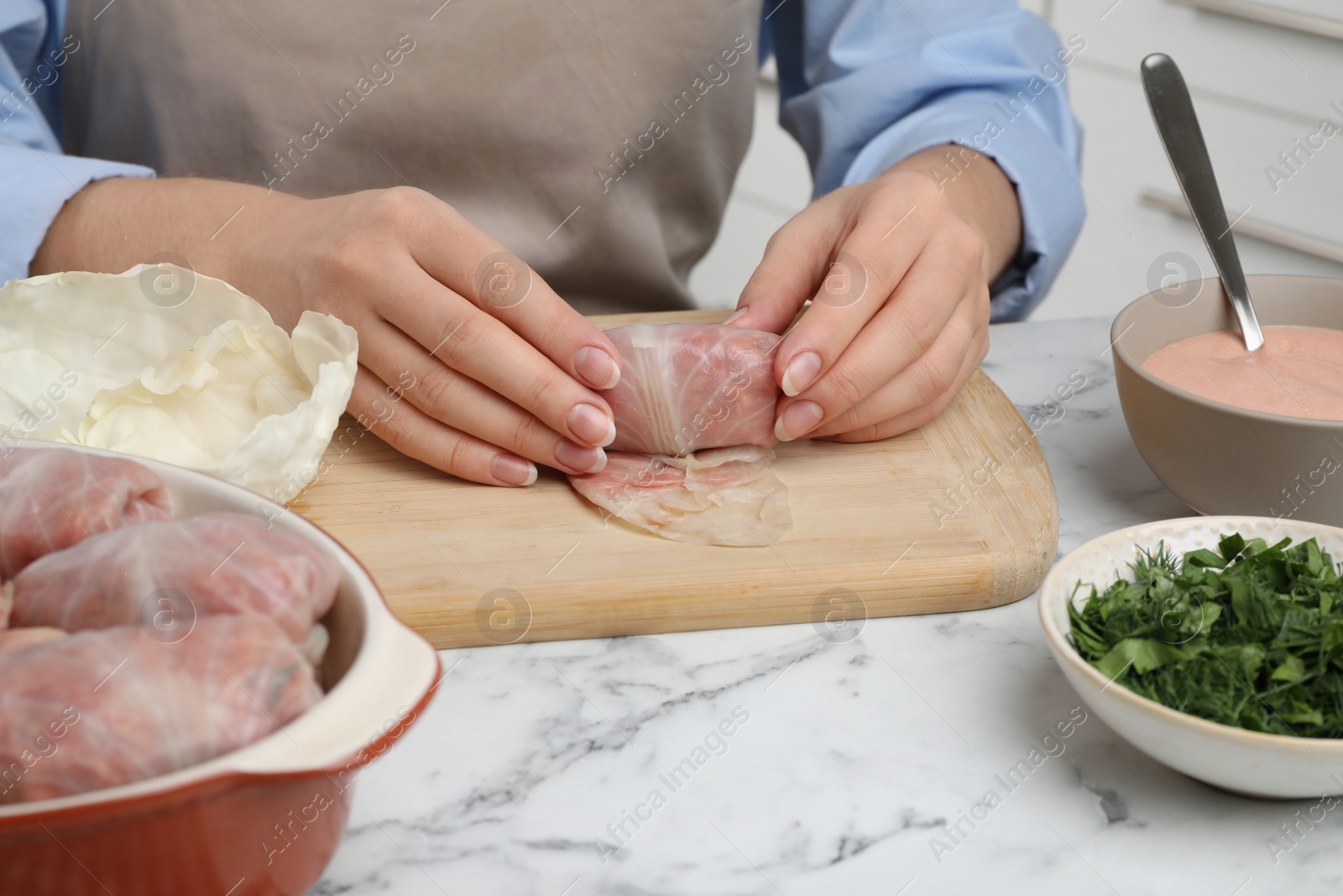 Photo of Woman making stuffed cabbage rolls at white marble table, closeup