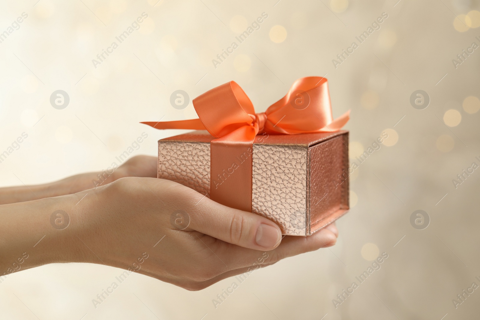 Photo of Woman holding beautiful gift box against blurred festive lights, closeup