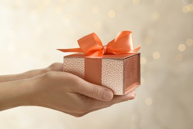 Woman holding beautiful gift box against blurred festive lights, closeup