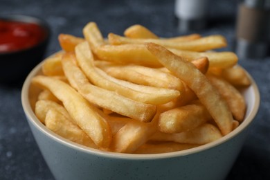 Photo of Delicious fresh french fries in bowl on black table, closeup