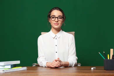 Photo of Portrait of beautiful young teacher sitting at table near chalkboard