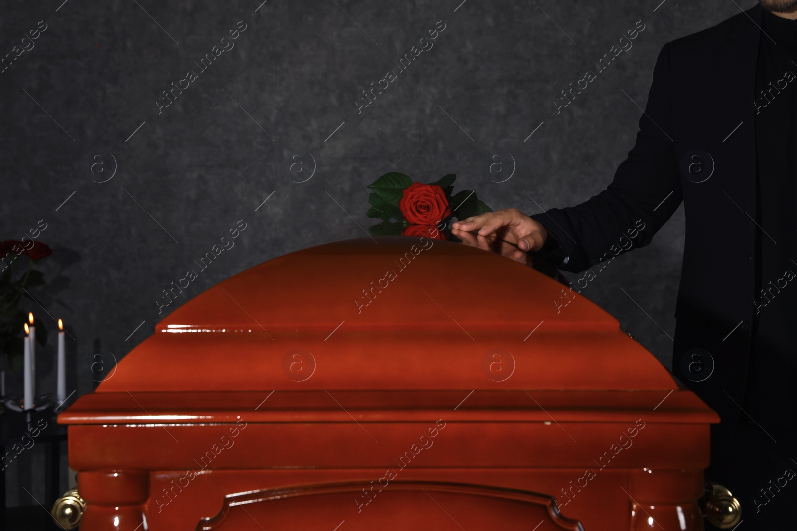 Photo of Young man near casket with red rose in funeral home, closeup