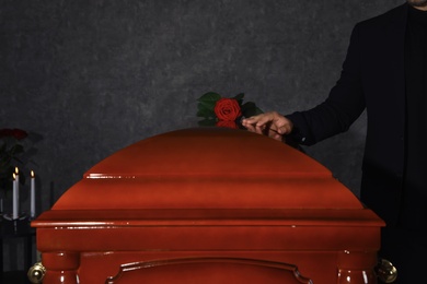 Young man near casket with red rose in funeral home, closeup