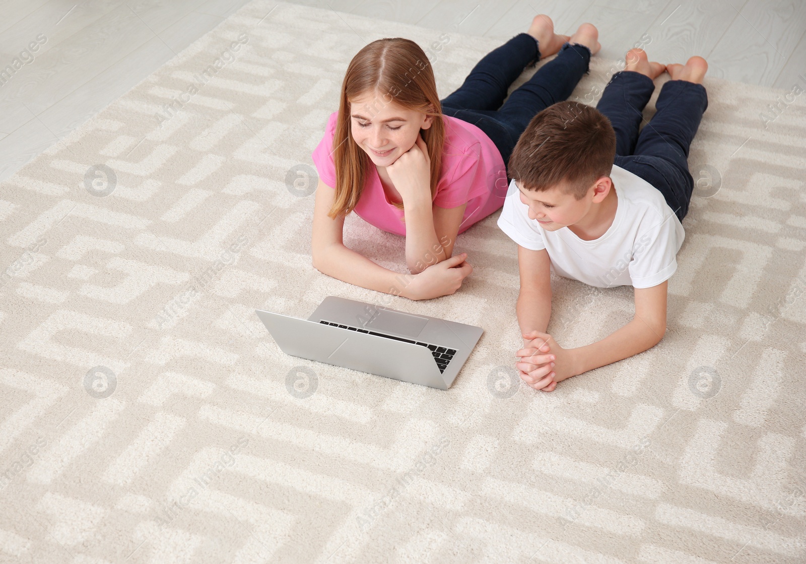 Photo of Teenage girl and her brother with laptop lying on cozy carpet at home