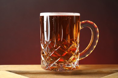 Photo of Mug with fresh beer on wooden crate against color background, closeup