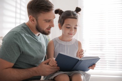 Little girl with father reading fairy tale indoors