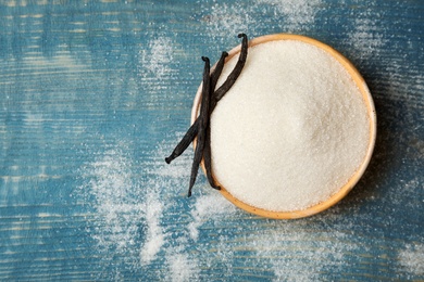 Photo of Bowl of aromatic vanilla sugar and sticks on wooden background