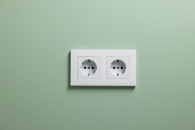 Electric power sockets on light green wall indoors