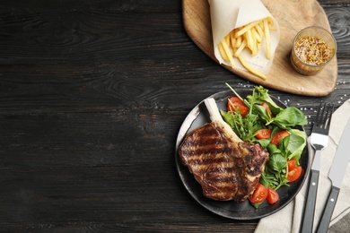 Flat lay composition with grilled beef steak on black wooden table, space for text