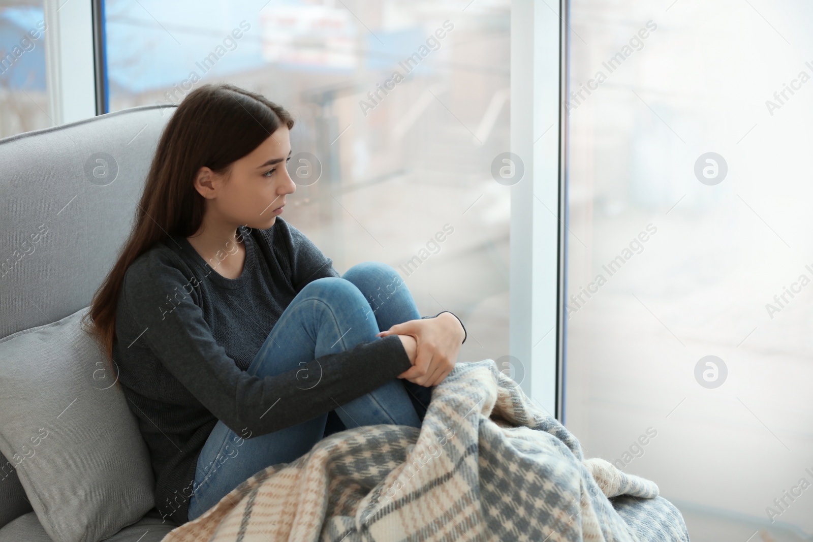 Photo of Upset teenage girl sitting at window indoors. Space for text