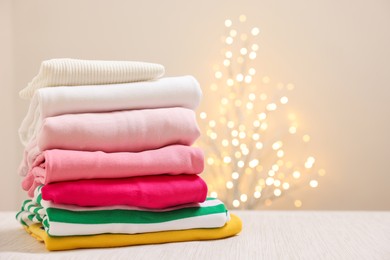 Photo of Stack of folded clothes on wooden table against beige background with blurred lights, space for text