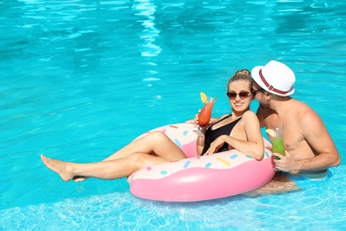 Photo of Young couple with refreshing cocktails and inflatable ring in swimming pool