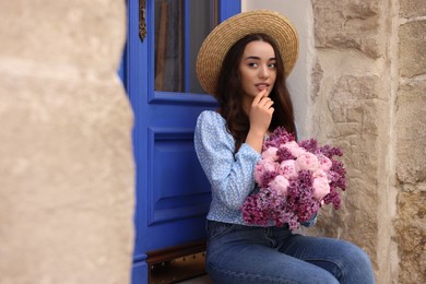 Photo of Beautiful woman with bouquet of spring flowers near building outdoors, space for text