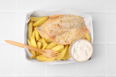 Photo of Delicious fish and chips with tasty sauce served on white tiled table, top view