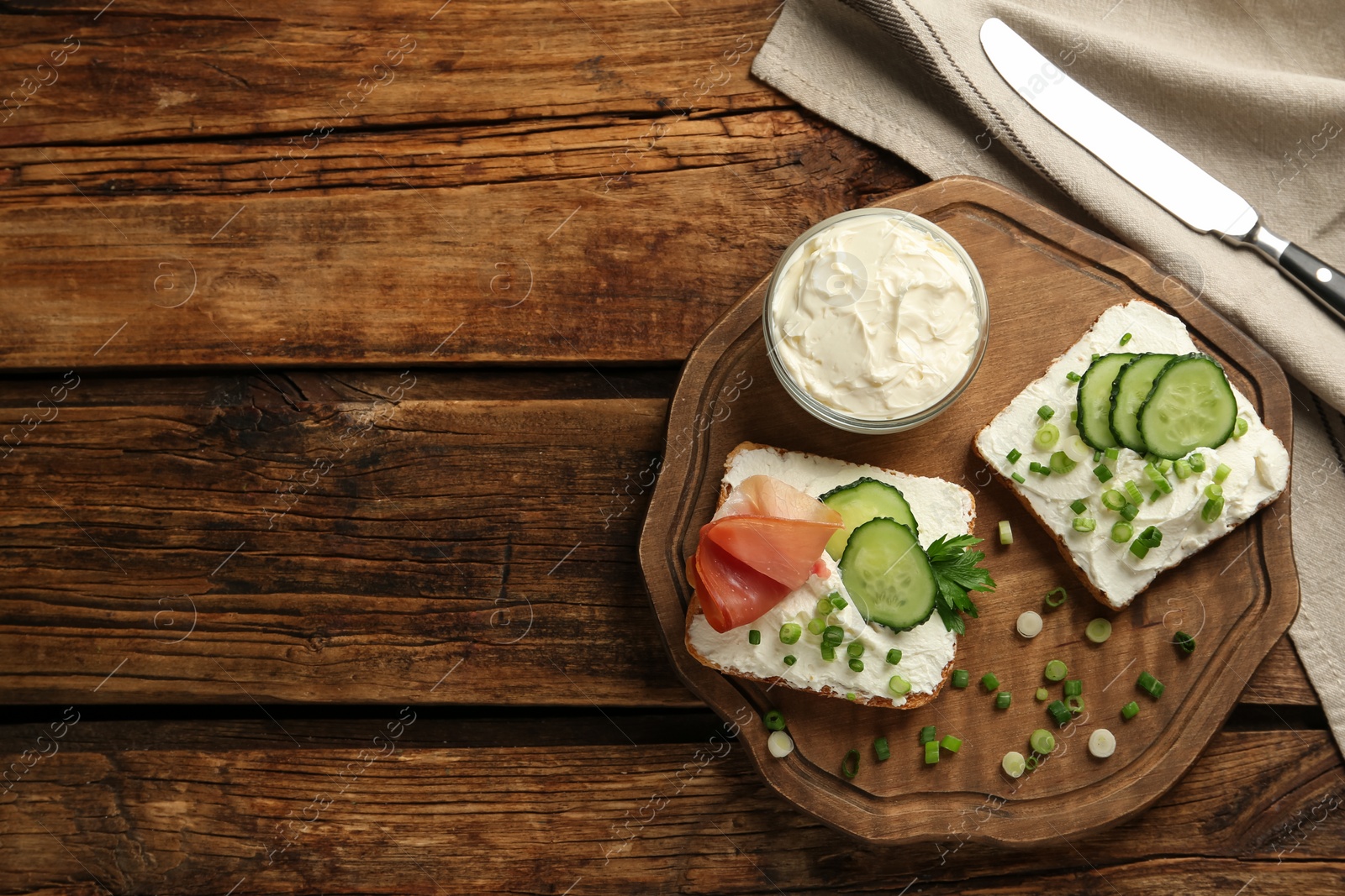 Photo of Delicious sandwiches with cream cheese and other ingredients on wooden table, flat lay. Space for text