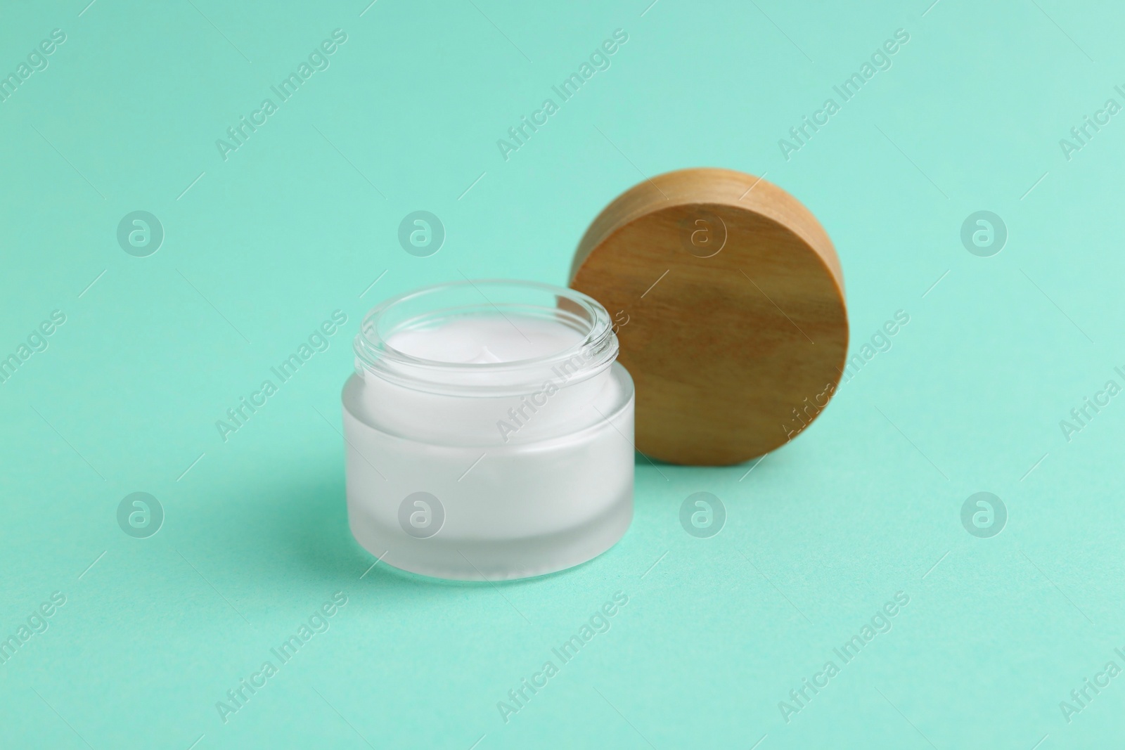 Photo of Moisturizing cream in open jar on turquoise background. Body care product