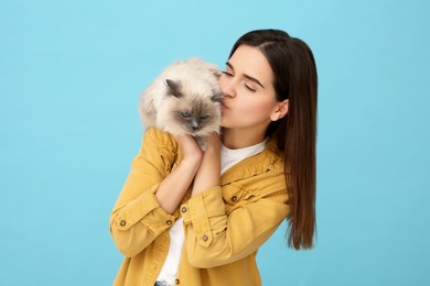 Woman kissing her cute cat on light blue background