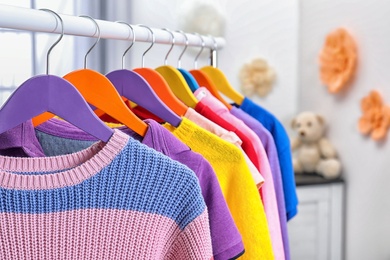 Colorful children's clothes hanging on wardrobe rack indoors, closeup