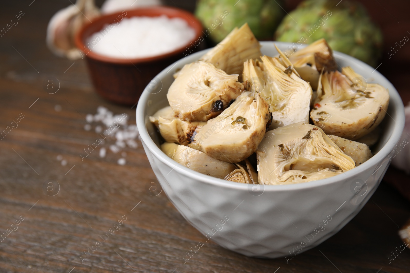 Photo of Bowl of pickled artichokes on wooden table, closeup