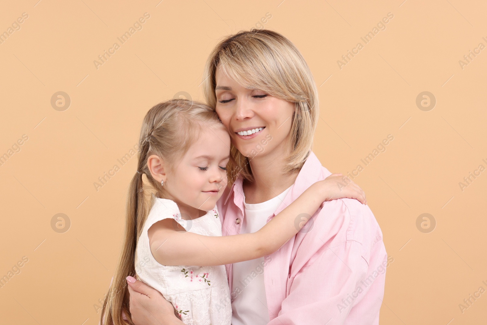 Photo of Daughter hugging her happy mother on beige background