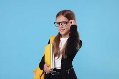 Happy schoolgirl with backpack and books on light blue background