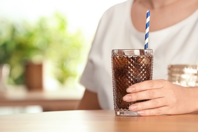 Photo of Woman with glass of tasty refreshing cola at table, closeup. Space for text