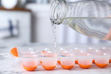 Photo of Pouring water into ice cube tray on white marble table, closeup