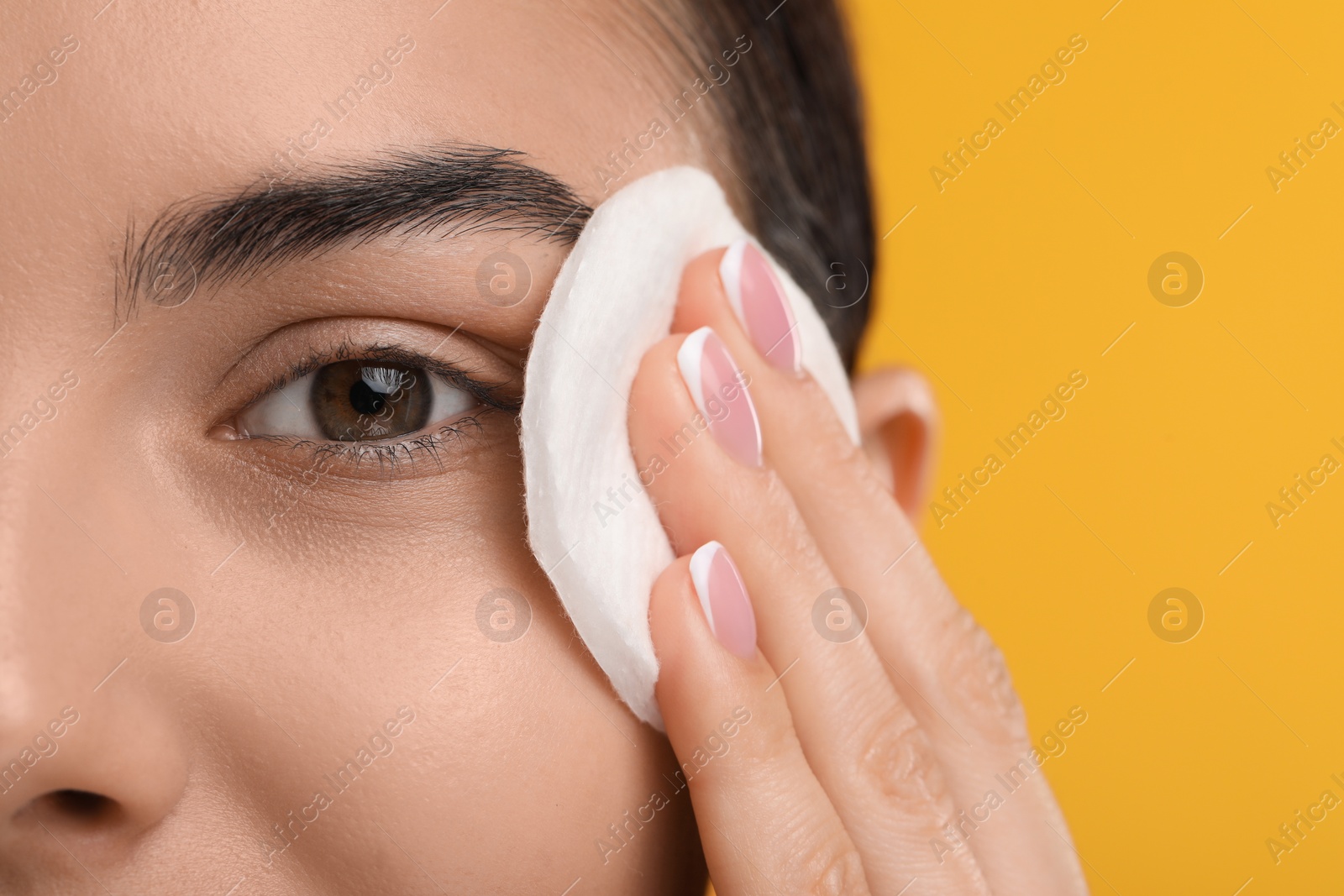 Photo of Beautiful woman removing makeup with cotton pad on orange background, closeup. Space for text