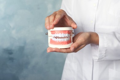 Photo of Dentist holding typodont teeth on light blue background, closeup. Space for text