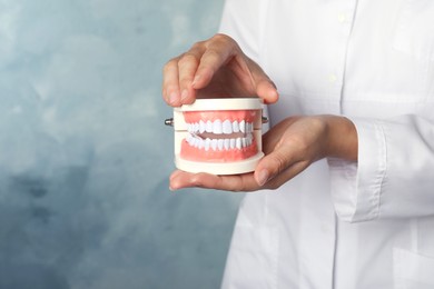 Dentist holding typodont teeth on light blue background, closeup. Space for text