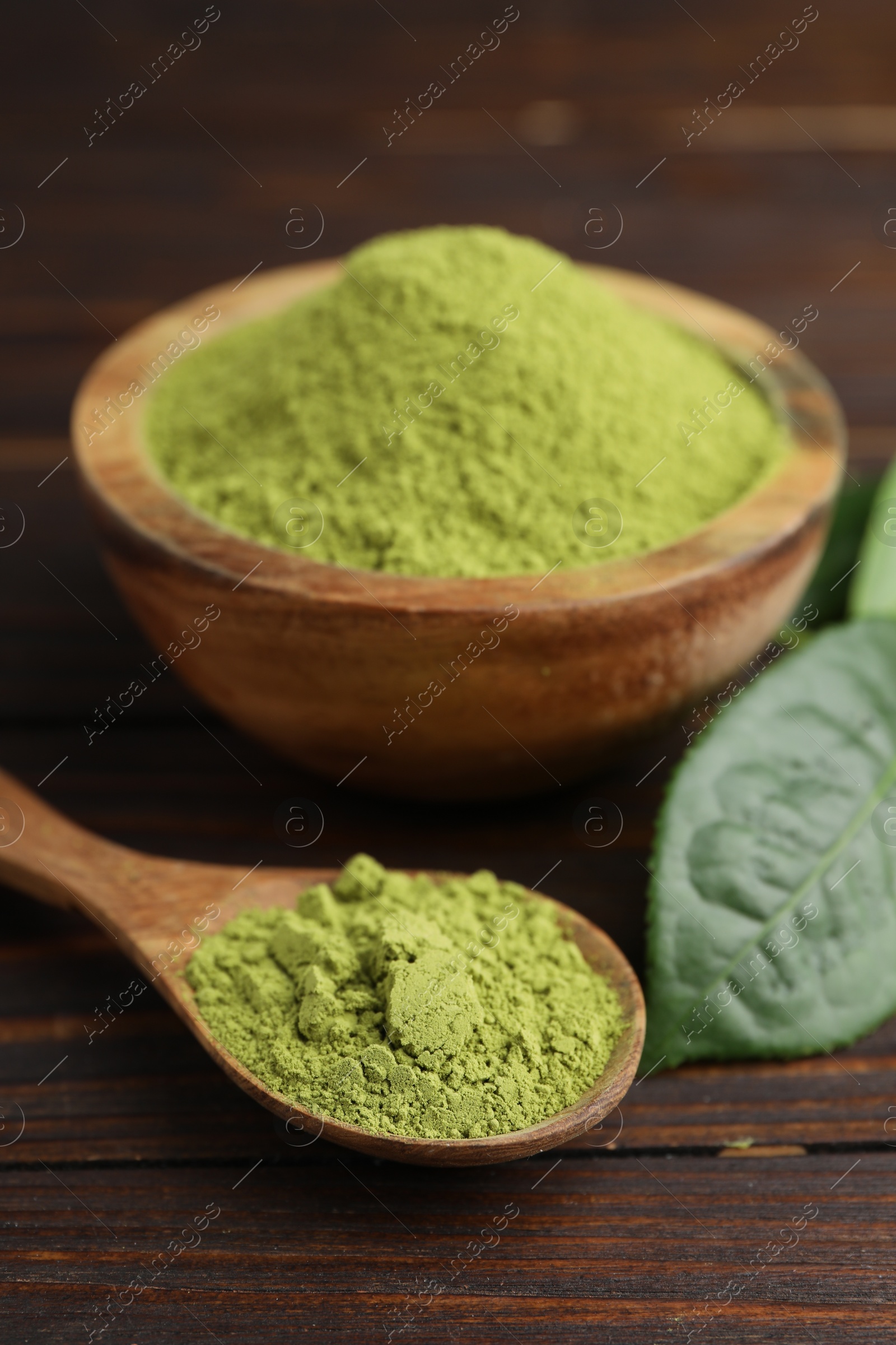 Photo of Bowl and spoon with green matcha powder on wooden table, closeup