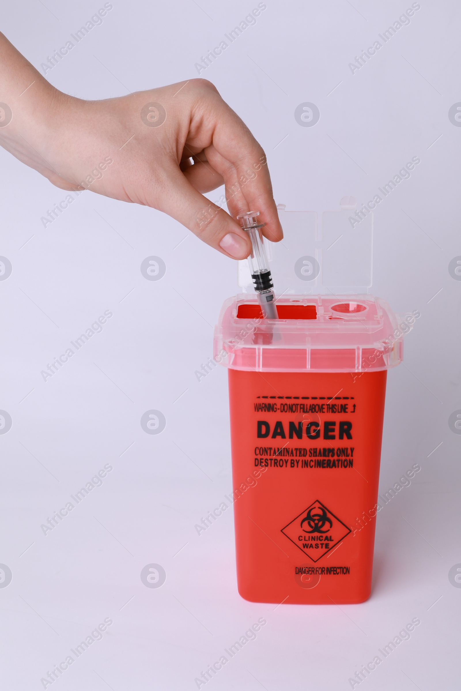 Photo of Woman throwing used syringe into sharps container on white background, closeup