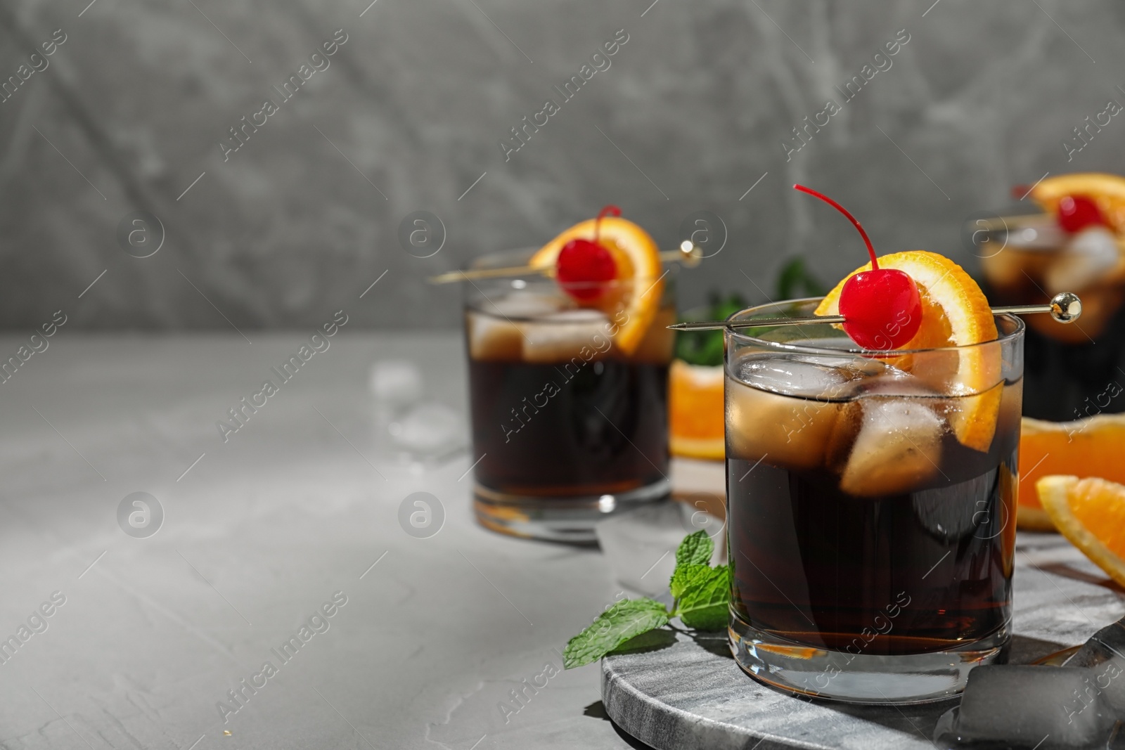 Photo of Glass of delicious cocktail decorated with cherry and orange on light grey table. Space for text