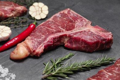 Fresh t-bone beef cut and different spices on light grey textured table, closeup