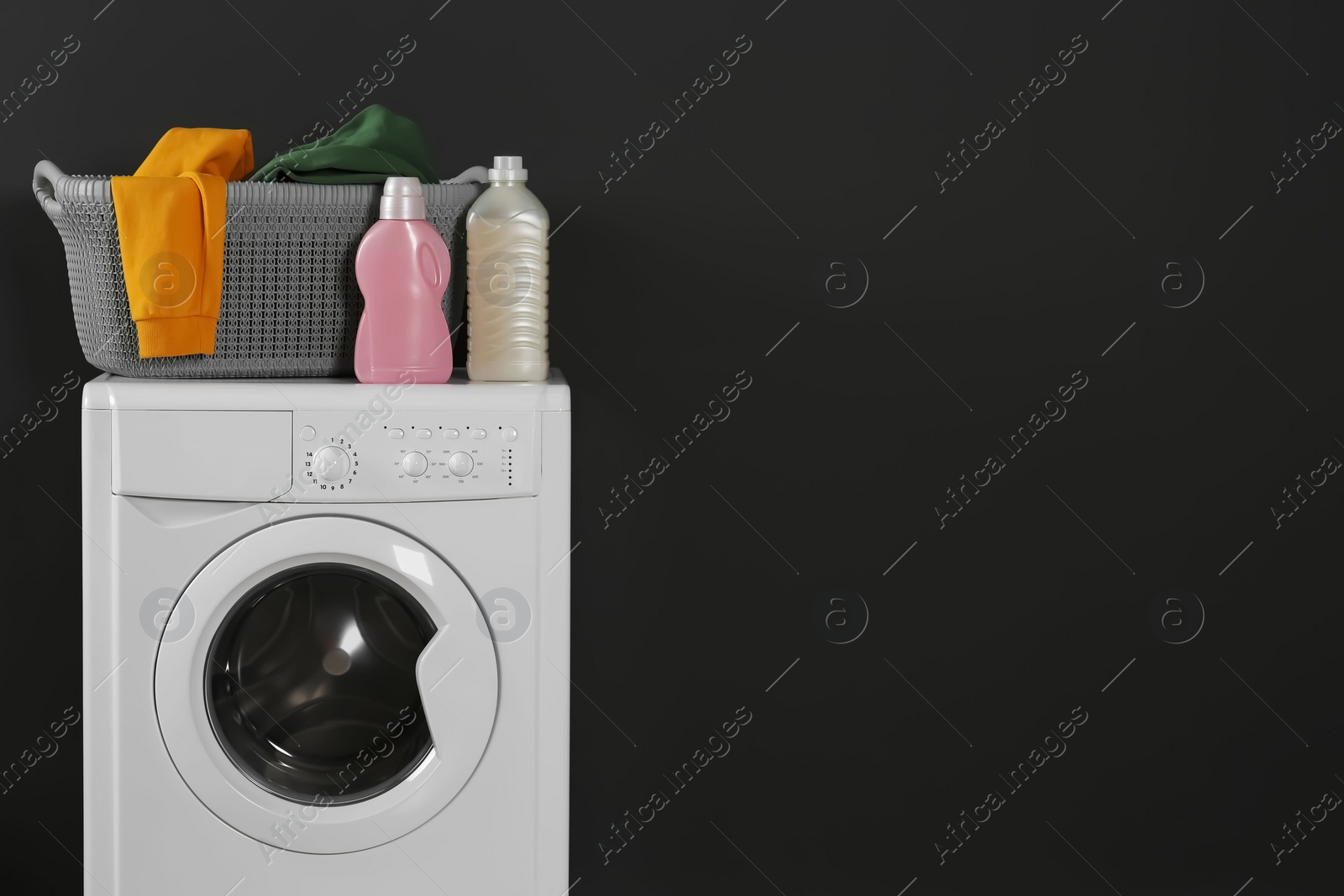 Photo of Washing machine with clothes and detergents on black background, space for text