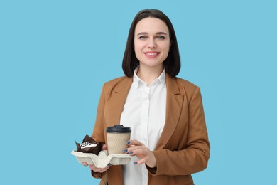 Photo of Happy young intern holding takeaway cup and muffin on light blue background