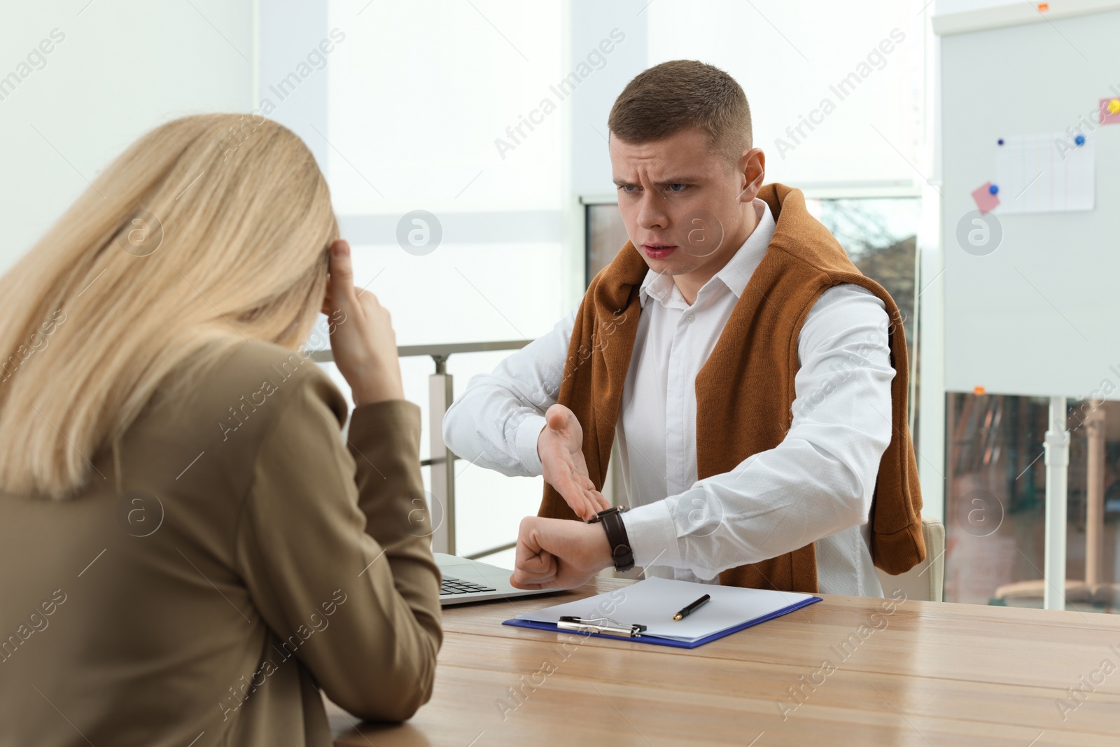 Photo of Businessman pointing on wrist watch while scolding employee for being late in office