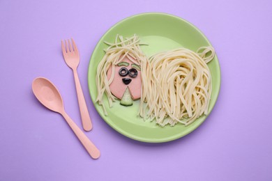 Photo of Creative serving for kids. Plate with cute dog made of tasty pasta, sausage and cucumber on violet table, flat lay