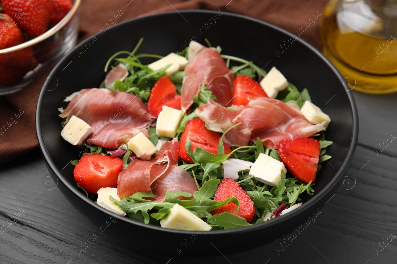 Photo of Tasty salad with brie cheese, prosciutto and strawberries on grey wooden table, closeup