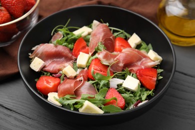 Photo of Tasty salad with brie cheese, prosciutto and strawberries on grey wooden table, closeup